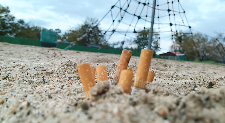 Zigarettenkippen stecken im Sand auf einem Spielplatz.