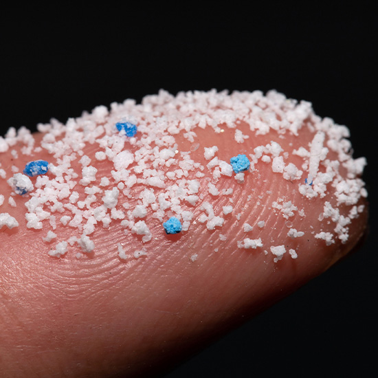 Winzige Mikroplastikpartikel in Nahaufnahme auf einem Finger vor schwarzem Hintergrund